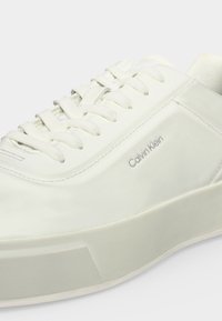 Λευκό αθλητικό παπούτσι Calvin Klein με χοντρή σόλα, σχέδιο με κορδόνια και διακριτικό λογότυπο στο πλάι.