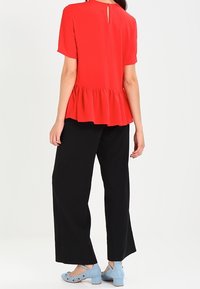 Rood T-shirt met korte mouwen, voorzien van een peplumontwerp en een sleuf aan de achterkant, gecombineerd met zwarte wijde broek en lichtblauwe instapschoenen met accenten.