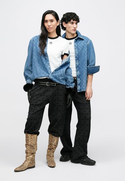 Farkkutakki, jonka alla valkoinen t-paita, jossa on ympyrälogo; yhdistetty mustiin kuvioituihin housuihin ja käärmekuvioisiin saappaisiin. Mukana mustat hansikkaat.