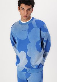 Blå sweatshirt med ett stort blommönster i olika nyanser av blått. Tillverkad av mjukt material med ribbade muddar och nederkant.