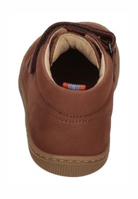 Braune Wildleder-Stiefelette mit einem weichen, gepolsterten Innenraum, einer beigefarbenen Fütterung und einer strukturierten Gummisohle. Verfügt über einen einzelnen Klettverschluss.