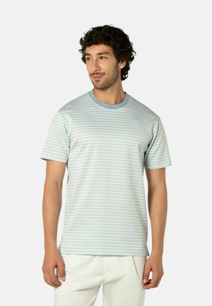 Mann mit lockigem Haar, der ein hellblau-weiß gestreiftes kurzärmeliges T-Shirt und weiße Hose trägt und leicht zur Seite schaut.