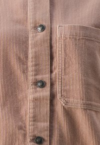 Pink corduroy shirt featuring vertical ribbing, dark buttons, and a single chest pocket for added detail. Textured, soft fabric.