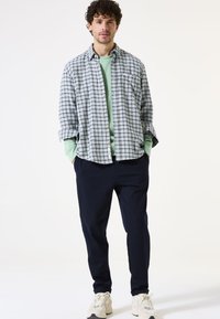 Geruite flanellen overhemd in blauw en groen, gelaagd over een mintgroene sweatshirt, gecombineerd met donkere broeken en beige sneakers.