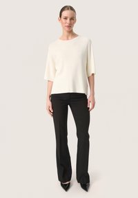 Cream short-sleeve top with a round neck, paired with black flared trousers, featuring a smooth texture and sleek silhouette.