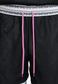 Pantalones cortos de malla negros con un patrón texturizado, que presentan una cintura blanca con detalles en negro y cordones rosa.