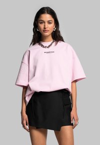 Oversized růžové bavlněné tričko s logem na přední straně, spárované s černou mini sukni se šňůrkami po stranách a kapsami pro praktičnost.
