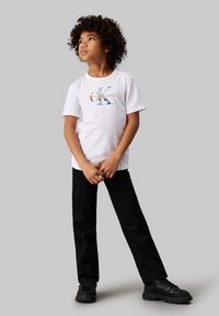 Camiseta de algodón blanca con logotipo azul y naranja, pantalones de mezclilla negros y botas negras. Textura suave y corte relajado.