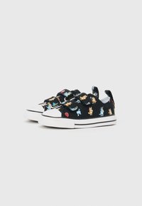 Svart kanvas sneakers med fargerike tegneserie dyremønstre, hvit gummitå, og justerbare stropper. Svarte og hvite stripete såler.