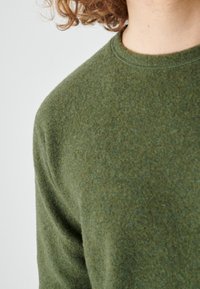 Green wool sweater with a soft, textured surface and a round neckline. The fabric appears warm and cozy with a subtle sheen.