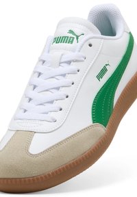 Weiße Sneaker mit grünem PUMA-Logo und Akzenten, ausgestattet mit einer Wildleder-Zehenkappe, strukturierten Gummisohlen und flachen weißen Schnürsenkeln.