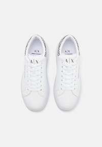 Zapatillas de cuero blanco con puntera redondeada, cordones planos y lengüeta texturizada. Presentan bordes con marca en negro alrededor del cuello.