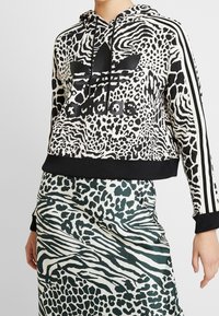 Felpa cropped in stampa animalier bianca e nera, con logo nero e strisce. Abbinata a una gonna verde e bianca a fantasia.