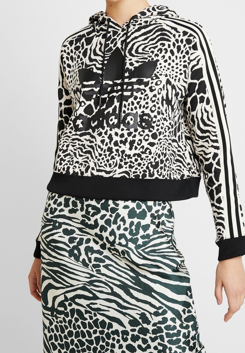 Felpa cropped in stampa animalier bianca e nera, con logo nero e strisce. Abbinata a una gonna verde e bianca a fantasia.