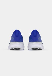 Siniset urheilukengät, joissa on verkkomateriaali yläosassa, valkoiset pohjat ja musta kumipohja. Ominaisuuksiin kuuluu vetotapit kantapäässä ja heijastavat yksityiskohdat.