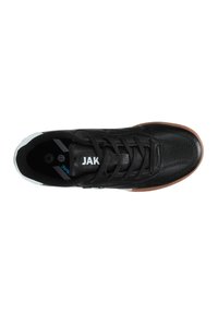 Sneaker nera in pelle con superficie texturizzata, chiusura con lacci e suola in gomma marrone. Presenta un accento bianco sul tallone e l'etichetta "JAK" sulla linguetta.