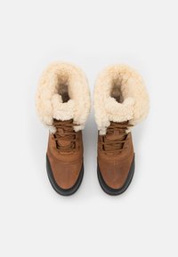 Botas marrones con cordones que cuentan con un suave cuello de piel sintética de color crema, un cuerpo de cuero liso y una suela de goma texturizada.