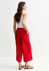 Pantalones anchos rojos de pierna amplia con cintura elástica, hechos de una tela ligera. Combinados con una camiseta blanca ajustada y sandalias marrones.
