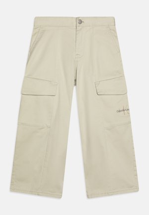 Bēša kokvilnas cargo bikses ar brīvu piegriezumu, divām lielām sānu kabatām un logotipa detaļu kreisajā augšstilbā. Aprīkots ar pogu aizdari.