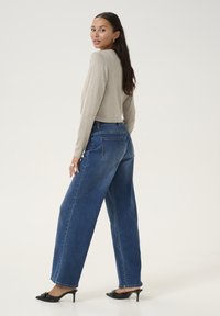 Világosszürke, cropped pulóver, magas derekú, sötétkék, bő szárú farmernadrág, elegáns fekete magassarkú mules, a modell hátulról látható.
