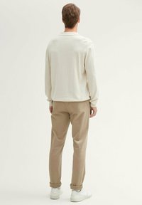 Beige long-sleeve shirt with a soft texture, paired with light brown, rolled-up trousers and white sneakers. View shows back of outfit.