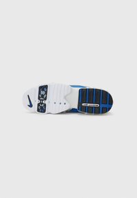 Semelle de basket Nike blanche et bleue avec des sections de bande de roulement noires et le logo "Zoom Air" sur un fond clair uni.