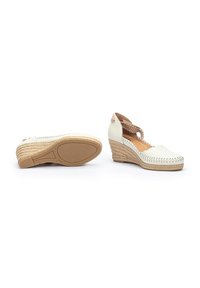 Espadrilles blanches à talon compensé avec des semelles en jute tressé, orteils ronds et motifs découpés. La cheville est ornée d'un détail de lien décoratif.