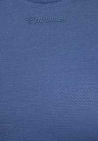 Niebieska koszulka sportowa z teksturowanej tkaniny o subtelnym wzorze i wytłoczonym logo przy dekolcie, stworzona z myślą o aktywności fizycznej.