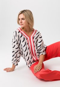 Blouse fluide noir et blanc à motif ondulé avec un col en V rose et des manches bouffantes, associée à un pantalon large corail éclatant.