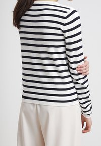 Pruhovaný svetr v bílé barvě s námořnickými vodorovnými pruhy, má kulatý výstřih a žebrovaný lem. Měkká pletenina, rukávy do poloviny délky.