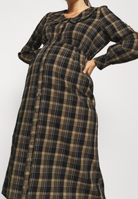 Robe de maternité à motif écossais marron et noir, avec un col arrondi, des manches longues et une fermeture boutonnée sur le devant, offrant une coupe ample.