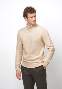 Beige polotröja i mjukt tyg, med långa ärmar, ribbade muddar och en åtsittande design. Matchad med mörkgrå byxor.