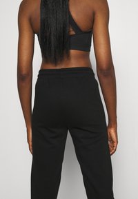 Svart sportbehå med ett korsat ryggdesign och texturerade remmar, i kombination med lösa svarta sweatpants med elastisk midja.