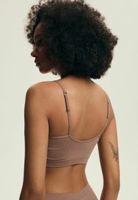 Fioletowy stanik ribbed z regulowanymi ramiączkami, gładką teksturą i okrągłym dekoltem, eksponujący tatuaż na ramieniu modelki.