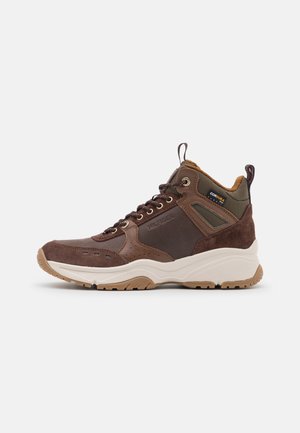 Bruine hoge sneaker met suède en stoffen panelen, witte zool, met het merk "Hilfiger" aan de zijkant en een Cordura stoffen label nabij de enkel.