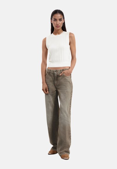 Top bianco a costine senza maniche abbinato a pantaloni beige larghi. Tessuto strutturato, gamba ampia e design classico a cinque tasche. Scarpe marroni.