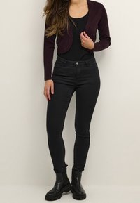 Cardigan corto bordeaux sopra un bodysuit nero, abbinato a jeans neri aderenti e stivali alla caviglia neri e chunky. Tessuto morbido e design aderente.