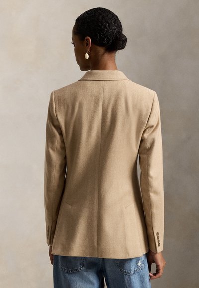 Rudos spalvos vilnonis švarkas su pritaikytu kirpimu, lapeliais su įpjova, viena nugara su ventiliacijos siūle ir užsegamais rankogaliais, derinamas su mėlynais nusidėvėjusiais džinsais.