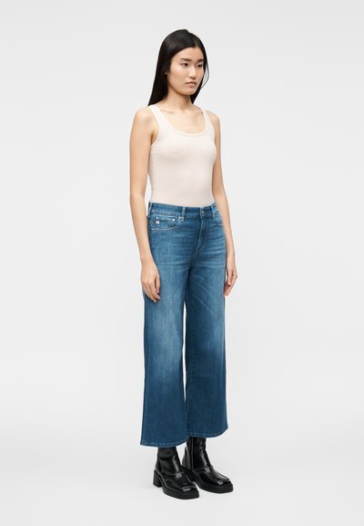 Canotta beige chiaro, jeans di denim blu a gamba larga a vita alta e stivaletti neri chunky. Tessuto liscio e vestibilità comoda.