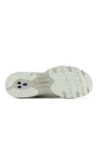 Vit texturerad gummisula med ett vågigt mönster, med tre blå ventilationshål och New Balance-logotyp i en central panel.