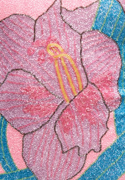 Κοντινή λήψη ροζ και μωβ χαντρών από λουλούδι ιβίσκου με κίτρινα στήμονες, περιγραμμένο με σκούρες χάντρες, σε φόντο από μπλε και πράσινες χάντρες.