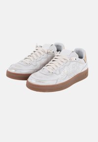 Zapatilla blanca con diseño perforado, acentos en beige, cordones planos y suela de goma marrón. Material superior suave con un brillo sutil.