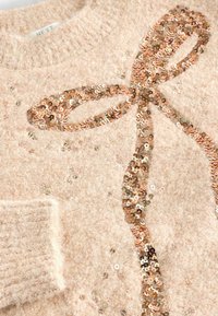 Roze donzige trui met een textuurafwerking, voorzien van een paillettenstrikontwerp in verschillende metallic tinten en een geribbelde manchette.