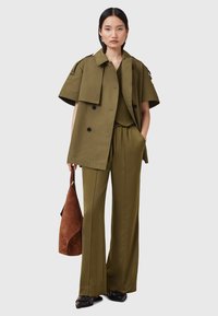 Oliwkowa, dwurzędowa marynarka z krótkimi rękawami na dopasowanej bluzce dzianinowej i szerokich spodniach. Brązowa torba ze zamszu dopełnia całość.