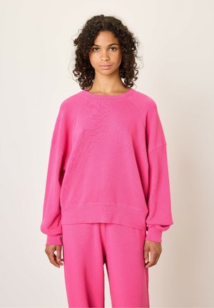 Sweatshirt surdimensionné fuchsia avec un col rond côtelé, des manches longues et un tissu texturé. Associé à un pantalon assorti pour un look complet.