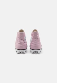 Zapatillas altas de lona rosas con suelas de goma blanca y una franja negra, con el clásico logo de Converse en la parte posterior.