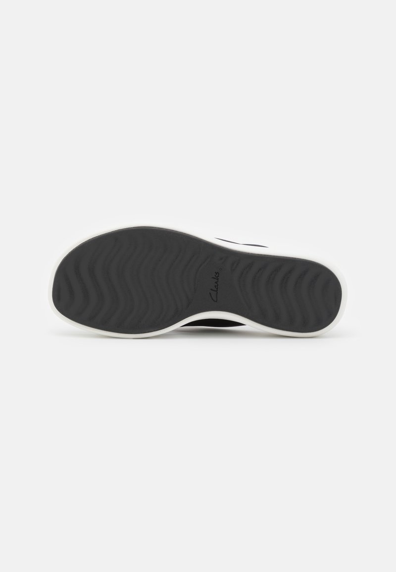 Suela negra de zapatilla con un patrón ondulado, con un borde blanco. Logo de Clarks visible cerca del talón. Caucho texturizado para mayor agarre.