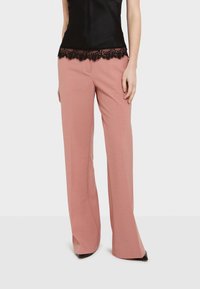 Roze wijde broek gemaakt van een gladde stof, met een zwarte kantafwerking op de taille. Gepaste pasvorm, met een strakke, minimalistische uitstraling.