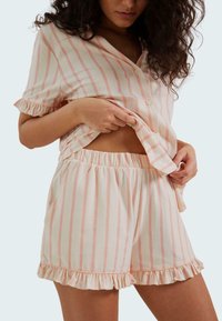 Ensemble de pyjama court à rayures roses et blanches avec des manches et un ourlet à volants, comportant des boutons sur la chemise et une taille élastique sur les shorts.