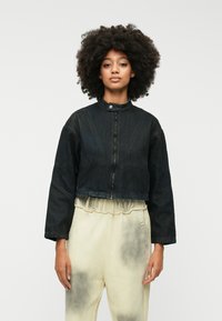 Skraćena crna traper jakna s visokim ovratnikom, prednjim zatvaračem i opuštenim rukavima. Uparena s svijetlim hlačama koje prikazuju izblijedjeli uzorak.